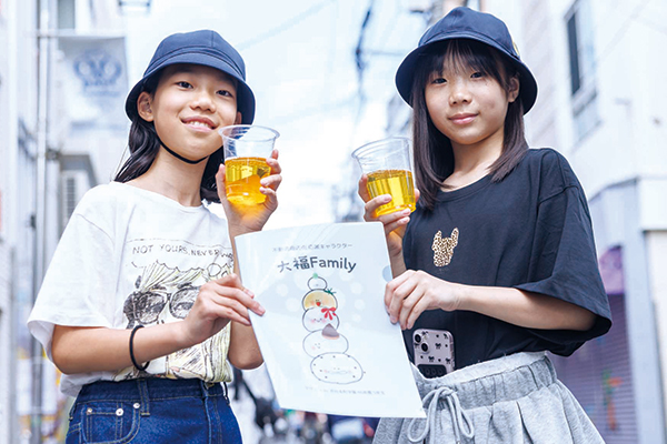 飲み物と不動通り商店街応援キャラクター「大福ファミリー」のファイルを手にした参加者たち