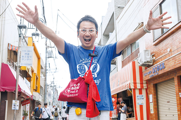 商店街の中央で手を広げポーズをとるレポーターの様子