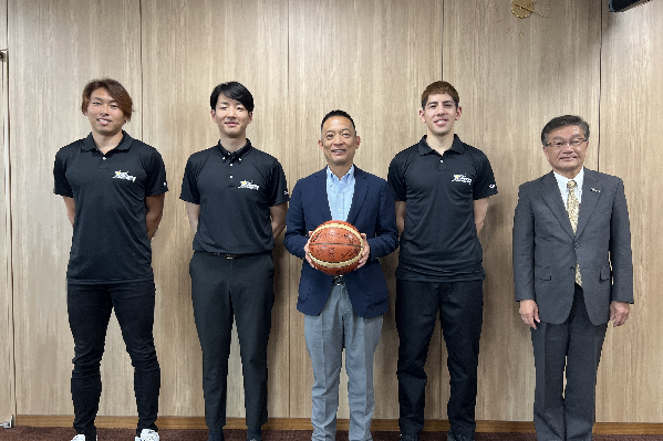 画像：サンロッカーズ渋谷の選手3人、バスケットボールを持った長谷部区長、サンロッカーズの浦長瀬正一社長が並ぶ様子