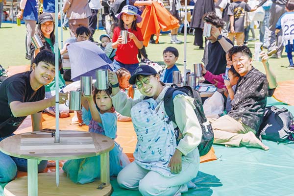 公園に集まってシートに座り飲み物を片手にくつろぐ参加者たち