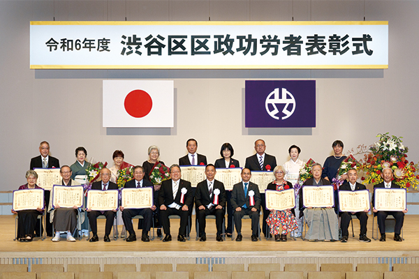 表彰式の様子。長谷部区長らと表彰状を掲げて座る功労者の皆さん。