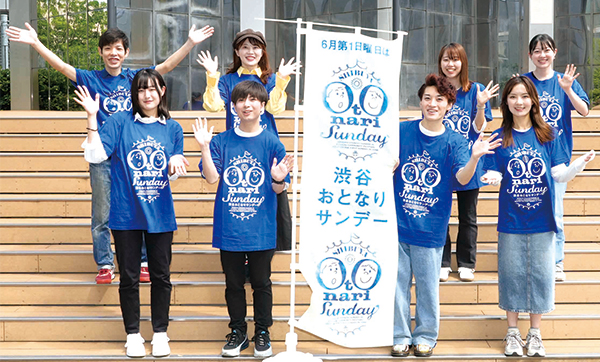 渋谷おとなりサンデーののぼり旗と撮影された青山学院大学の皆さんの記念写真