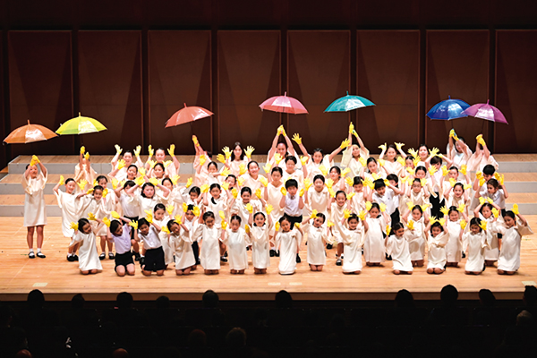 過去の演奏会の様子。黄色い軍手をはめて傘を頭上に掲げている子どもたち