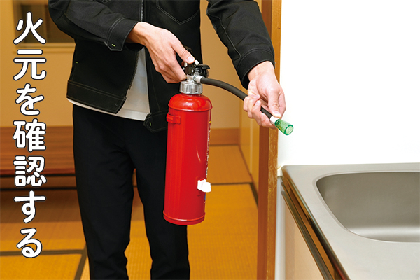 消火器を持って火元にノズルを向けている