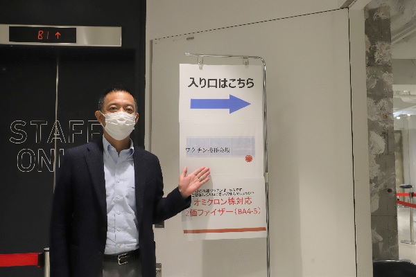 「西武渋谷店モヴィーダ館」の新型コロナワクチン接種会場の前に立っている長谷部区長の様子の写真