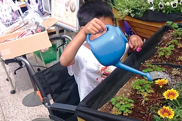 プランターの草花に水をあげる車いすユーザー